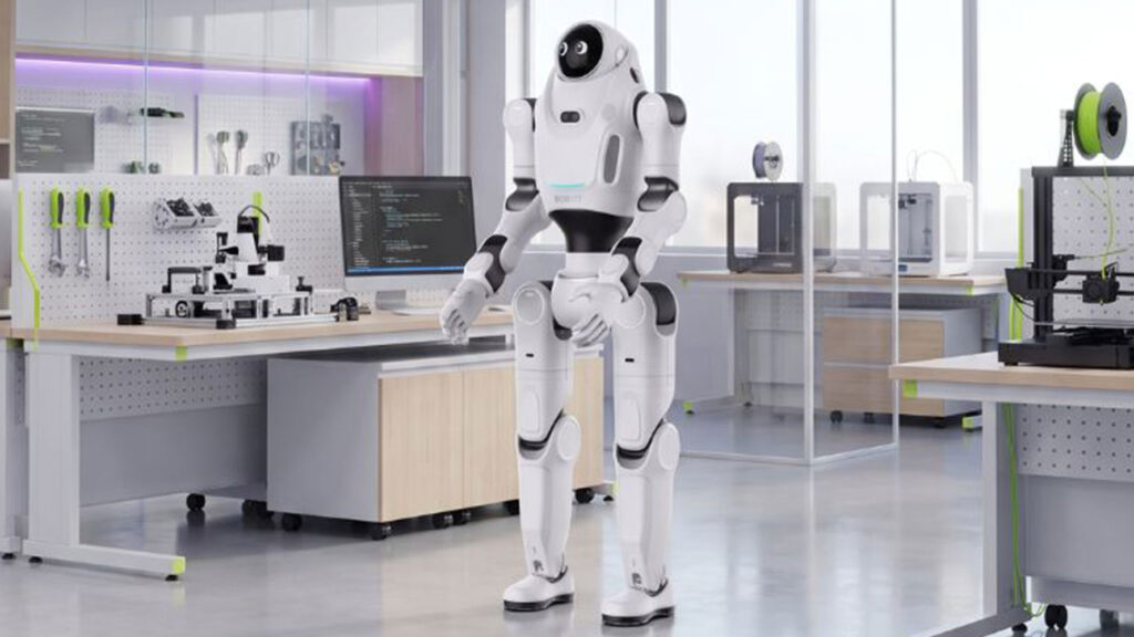 Ein weißer humanoider Roboter steht in einer hell beleuchteten Werkstatt, die mit 3D-Druckern und Computerarbeitsplätzen ausgestattet ist.